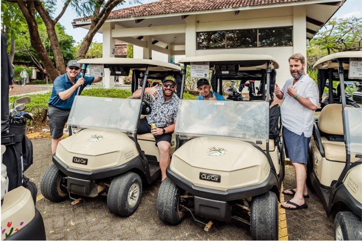 Golfers standing with 2 golf carts waving to the camera