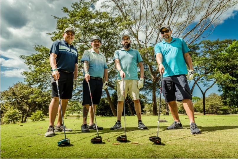 4 Golfers pointing their clubs toward the camera which is positioned near the floor